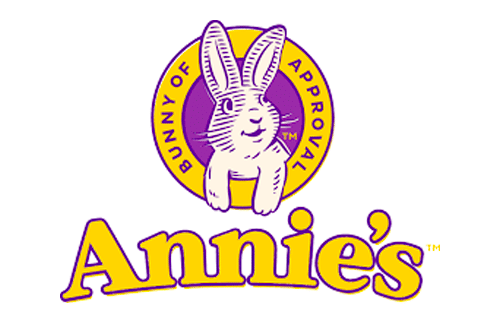 Logo for Annie’s featuring a white bunny inside a yellow and purple oval with the words “Bunny of Approval.” Below the oval, “Annie’s” is written in large, yellow letters outlined in purple.