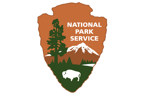 The National Park Service logo shaped like an arrowhead, featuring a green tree, mountains, a lake, grass, and a white bison, with "National Park Service" written in white at the top.